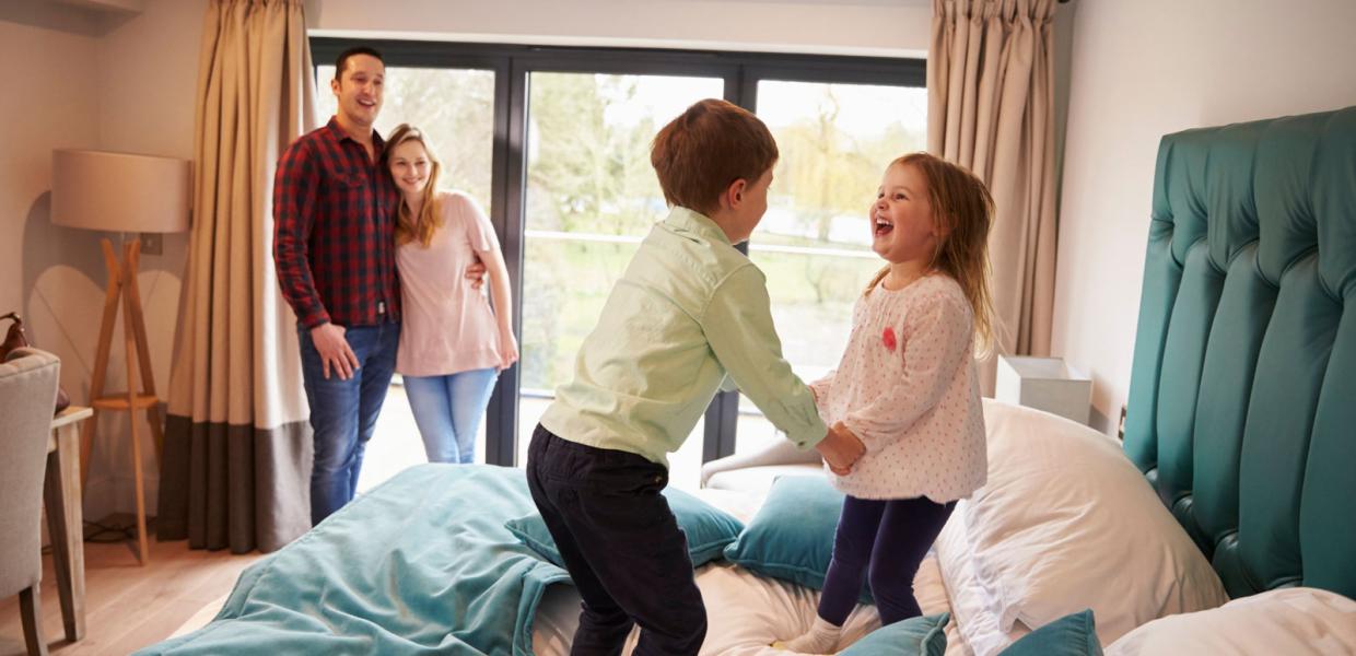 Zwei Kinder springen mit viel Spaß auf dem Bett herum, während Mama und Papa ihnen entspannt dabei zusehen. Im LEGOLAND® Billund Resort gibt es viele verschiedene Arten von Übernachtungsmöglichkeiten.