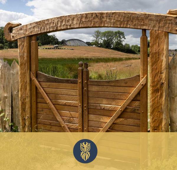 Ein geschnitztes Holztor zum Lejre Land der Legenden. Das Tor ist aus starken Balken mit einem Schlangenkopf an jedem Ende des darüber liegenden Balkens gebaut.