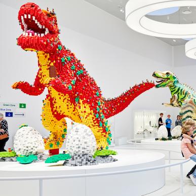 Betrachtet die faszinierenden Riesendinosaurier in der LEGO® House Masterpiece Galerie. Viele machen hier das Gleiche wie diese Familie hier und machen ein Selfie oder ein Porträtfoto mit einem wilden Dinosaurier im Hintergrund. 