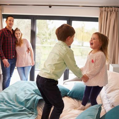 Zwei Kinder springen mit viel Spaß auf dem Bett herum, während Mama und Papa ihnen entspannt dabei zusehen. Im LEGOLAND® Billund Resort gibt es viele verschiedene Arten von Übernachtungsmöglichkeiten.