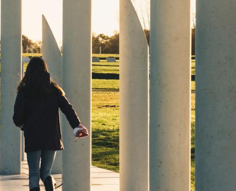 Eine Person geht entlang der weißen Betonpfeiler, die den Verlauf der Palisade um die Festung von Gorm dem Alten zeigen.