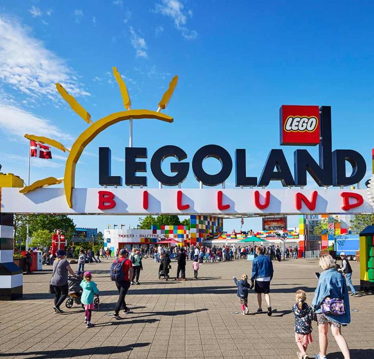 Das Eingangstor zum LEGOLAND mit den zwei Türmen aus LEGO® Steinen. Zahlreiche Gäste strömen in den Park, um diesen an einem Sommertag unter blauem Himmel zu genießen.